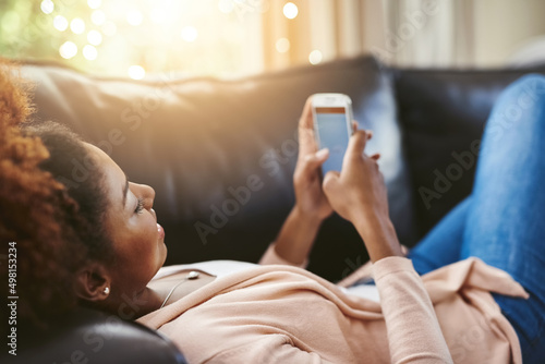 Taking it easy. High angle shot of an attractive young woman using her cellphpone while chilling at home on the sofa.