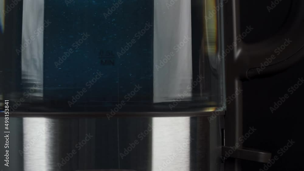 A person's fingers press the button of a glass kettle to boil water. Bubbles are rising in the blue light. low motion. A person's fingers press the button of a glass kettle to boil water. Bubbles are rising in the blue light. low motion.