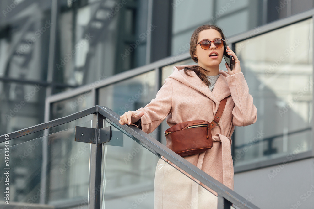 Woman in pink dress talking to smarthone outdoor on grey urban city background