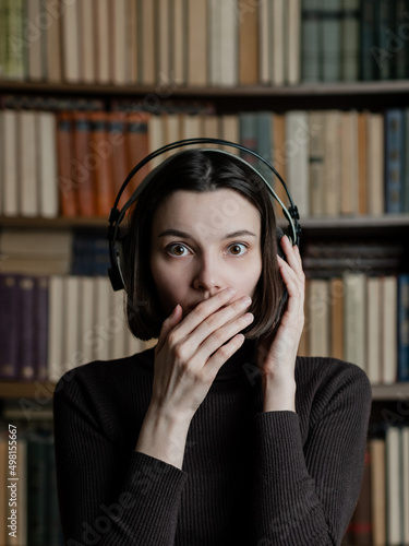 Woman in headphones listening to audiobooks on background of library shelves with paper books