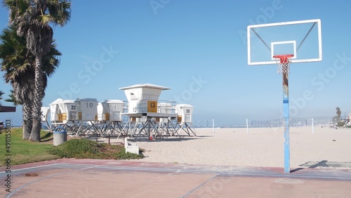 Palm trees and basketball sport field or court on beach, California coast, USA. Streetball playground on shore and lifeguard stand, tower ot station. Mission beach, San Diego. Hoop, backboard and sky.