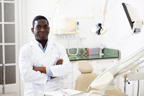 Smiling african-american man orthodontist wearing white coat and looking at camera.