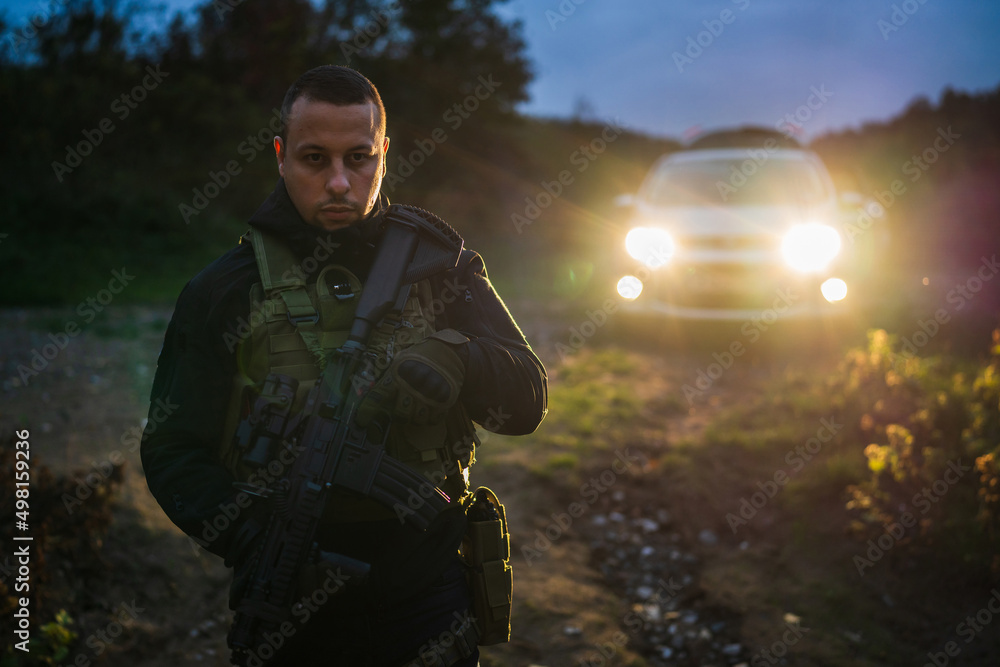 Special force police or army or private security soldier holding automatic rifle while standing in front of the vehicle at night copy space