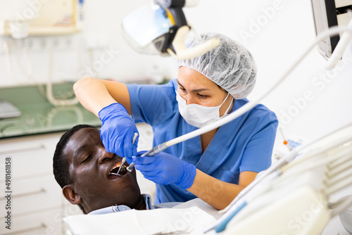 Confident woman stomatologist treating teeth to african american patient in modern dental office..