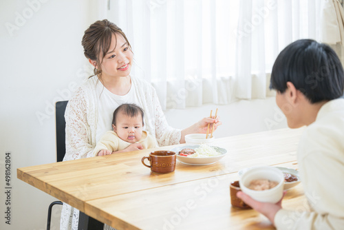 食卓で赤ちゃんと一緒にご飯を食べるママさんとあやすパパさん