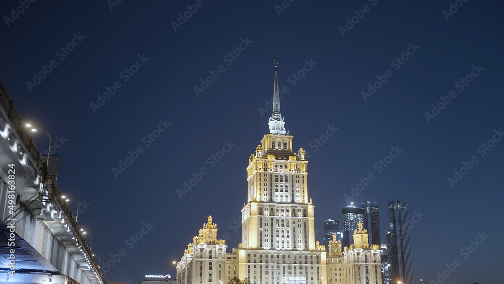 Late night cityscape with illuminated skyscraper in Moscow designed in the Stalinist style. Action. Sailing under the bridge and revealing beautiful building on a dark blue evening sky background