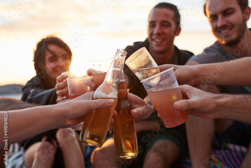 Young, wild and free. Shot of a group of happy young friends toasting with their drinks while relaxing on the beach.