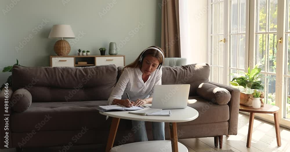 Young 35s attractive woman studying at home use headphones laptop and video call application, listen on-line teacher taking notes, improve foreign language knowledge distantly. Videocall event concept Young 35s attractive woman studying at home use headphones laptop and video call application, listen on-line teacher taking notes, improve foreign language knowledge distantly. Videocall event concept