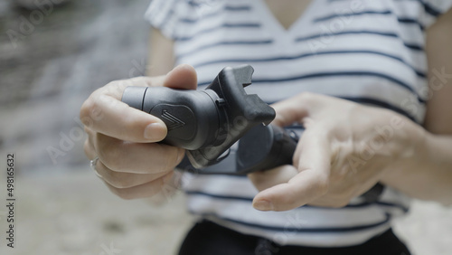 Close up of female hands holding smartphone tripod on blurred natural background. Action. Woman unfolding tripod.