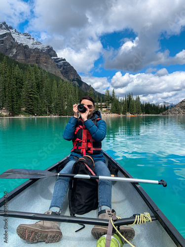 Woman in canoe in middle of Moraine Lake taking pictures with digital camera