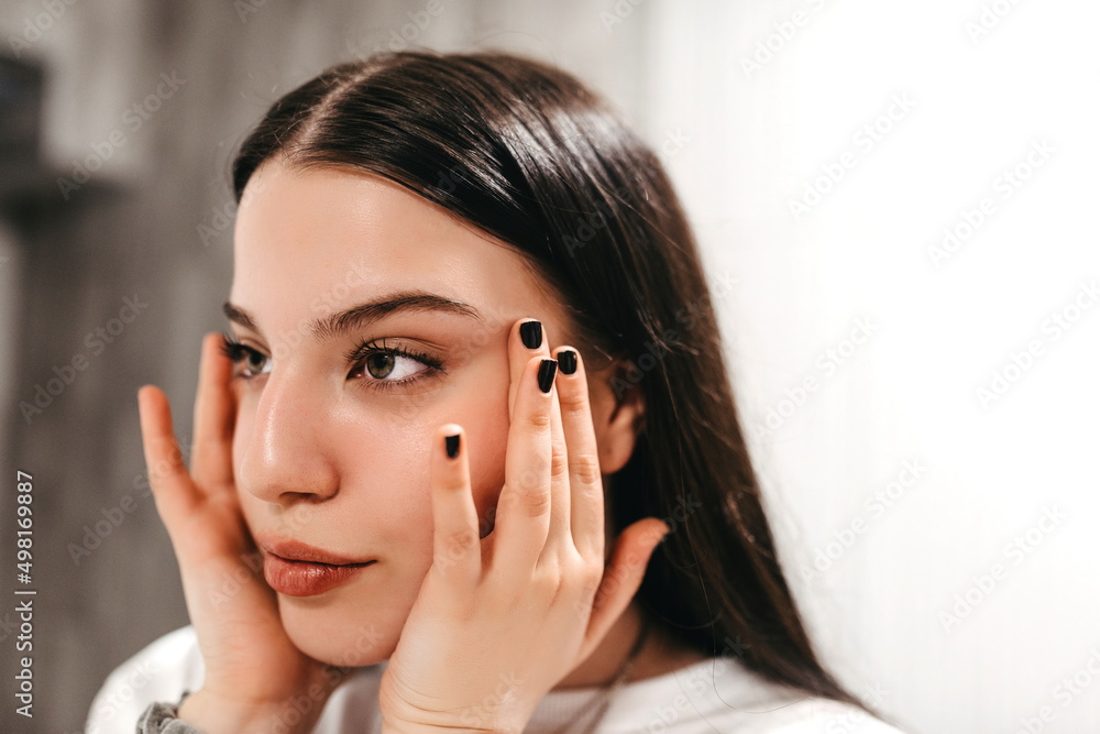 Skin care. Close up of young woman touching her face to apply moisturizer. White background Skin care. Close up of young woman touching her face to apply moisturizer. White background