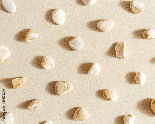 Aesthetic minimal pattern with set of pebble stones on fine sand background. Top view on natural stone neutral beige color. Summer concept