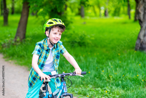 A boy with a green bicycle helmet on his head rides his bicycle in the summer park. Summer rest
