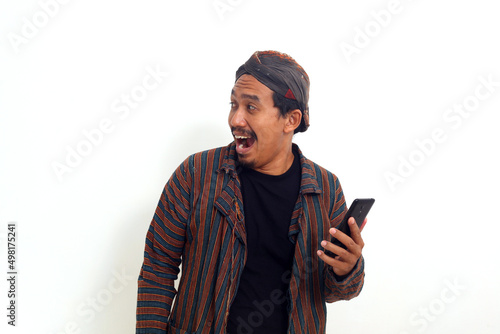 Asian man in javanese traditional costume standing while holding a phone. Isolated on white © SetianingDyah