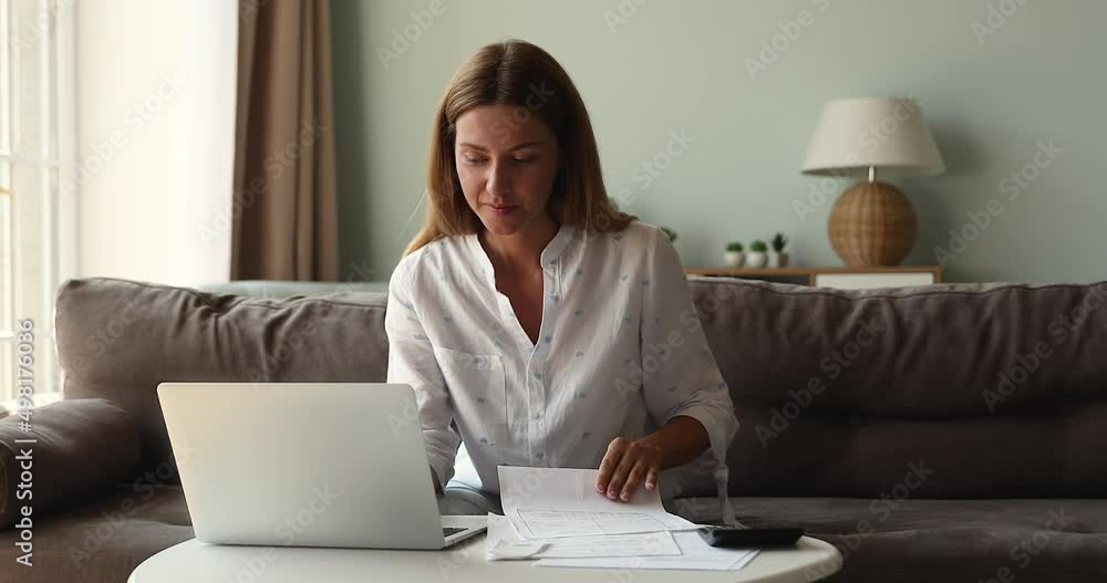 Young beautiful woman housewife sit on sofa at home, pay household bills on-line use secure e-bank application on laptop, analyze expenses, earnings feels satisfied smile manage family budget concept Young beautiful woman housewife sit on sofa at home, pay household bills on-line use secure e-bank application on laptop, analyze expenses, earnings feels satisfied smile manage family budget concept