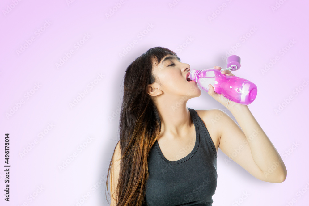 Young woman drinks water after exercise on studio Young woman drinks water after exercise on studio