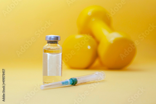 syringe lies next to a jar of liquid and dumbbells on a yellow background, horizontal picture, copy space. the concept of doping in sports, steroids, testosterone and other drugs banned in sports.