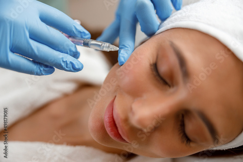 Closeup of young woman receiving hyaluronic acid injection in cheekbones at beauty salon. photo