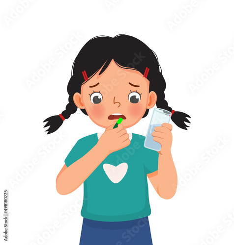 cute little girl taking a medicine capsule with a glass of water