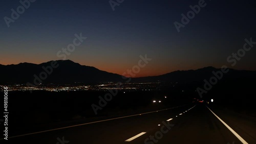 Car driving on desert road at night, freeway or highway in twilight dusk, perspective view thru windscreen or windshield. Road trip in California USA. Valley and mountains on horizon, dividing line.