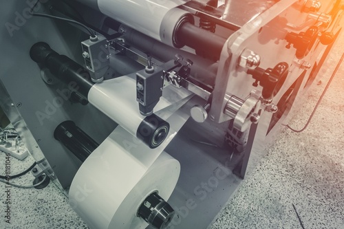 Roller of white printing paper for self-adhesive label on the shaft of the die-cutting machine in the printing house. Selective focus