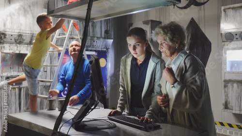 Grandmother and granddaughter uisng computer in escape room to solve conundrum. Grandfather and grandson standing in background and looking at map. photo