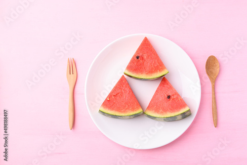 Sliced watermelon on plate with wooden spoon and fork on pink color background, Tropical fruit in summer season, Top view