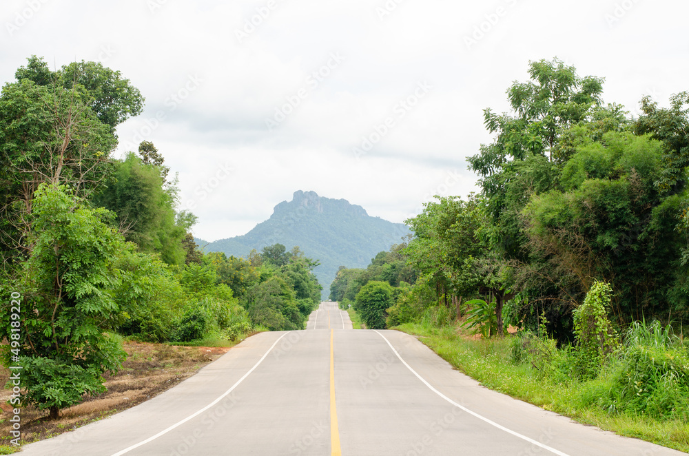 An empty highway undulating road among the green trees and the huge mountains in front at Lampang, Thailand