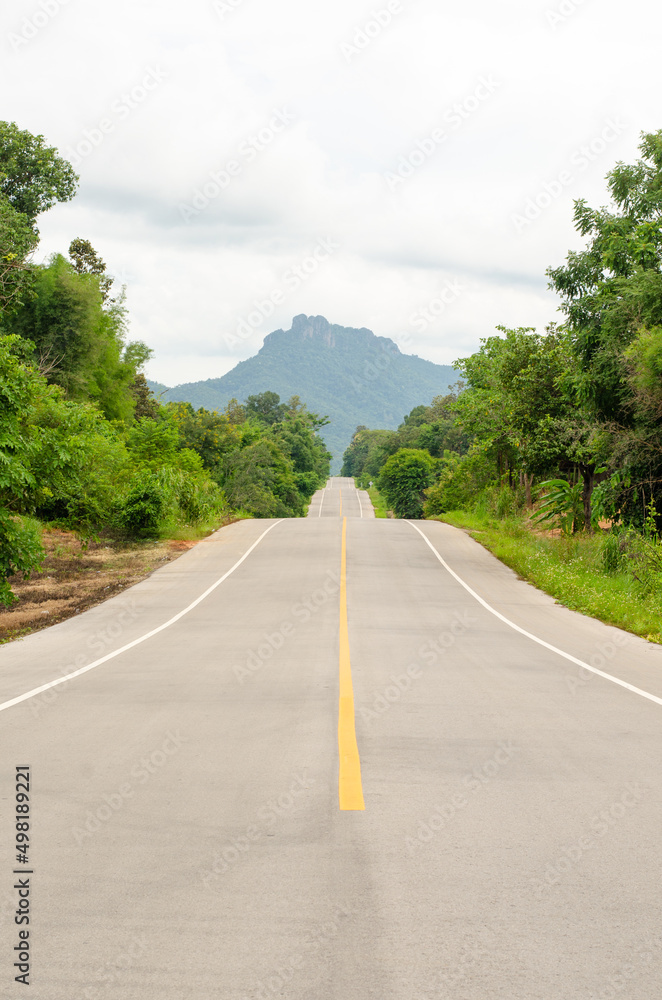 An empty highway undulating road among the green trees and the huge mountains in front at Lampang, Thailand