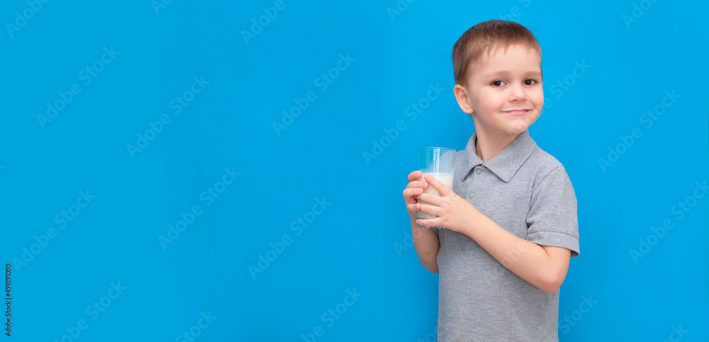 Banner. Cute boy 5-6 years old drinking milk on colored blue background. He knows that he needs to drink milk for bone health. The baby loves milk. Concept of children's healthy nutrition Banner. Cute boy 5-6 years old drinking milk on colored blue background. He knows that he needs to drink milk for bone health. The baby loves milk. Concept of children's healthy nutrition