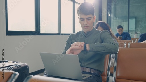 Young handsome man with a suitcase sitting working his laptop at airport terminal hall while waiting landing for her flight, tourist men in international airport, travel trip