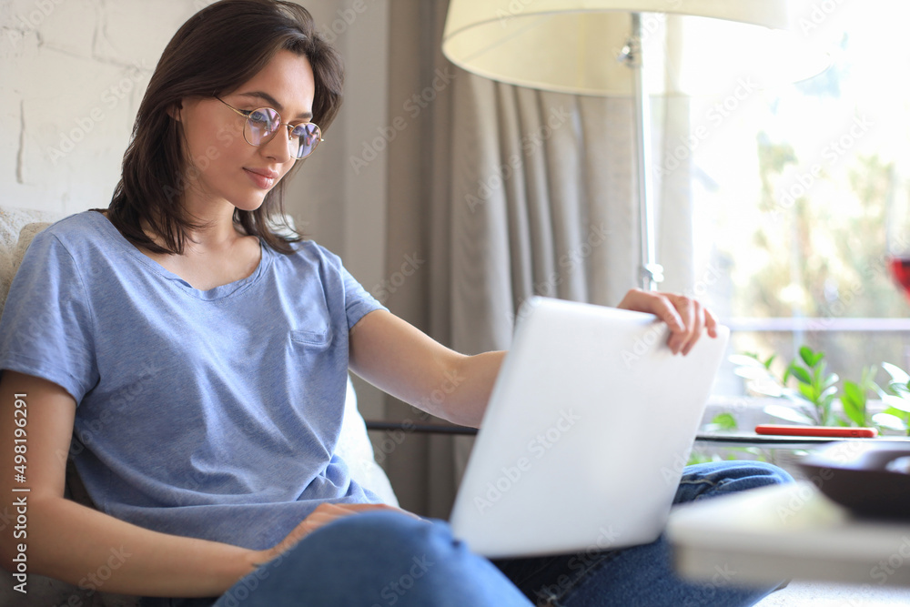 Smiling young woman sitting on sofa with laptop computer and chating with friends. Smiling young woman sitting on sofa with laptop computer and chating with friends.