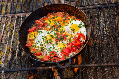 Eggs prepared with vegetables on a frying pan on the fire in the forest. Cooking scrambled eggs over an open fire. Breakfast in nature. Tourist food.