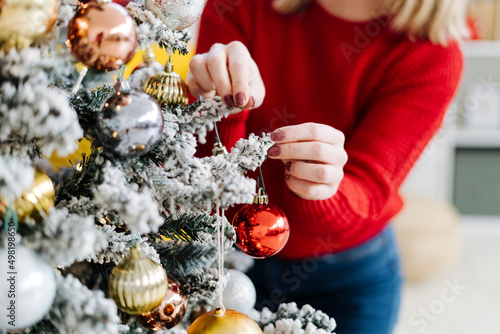 Woman decorating Christmas tree with bauble at home photo