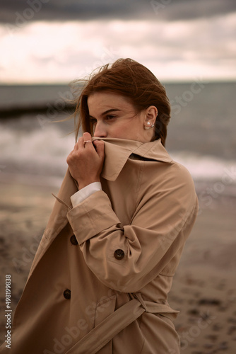 Woman covering face with trench coat at sunset
