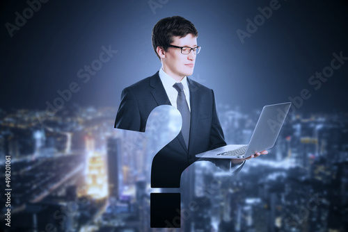 Abstract attractive european businessman with laptop and question mark shape on night city background. FAQ and answer concept.