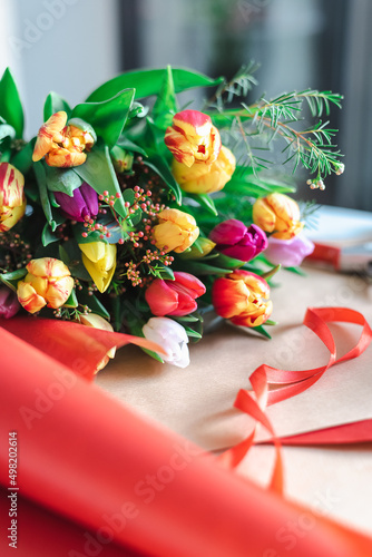 A colorful bouquet of spring tulips lies on a bright red wrapping paper.