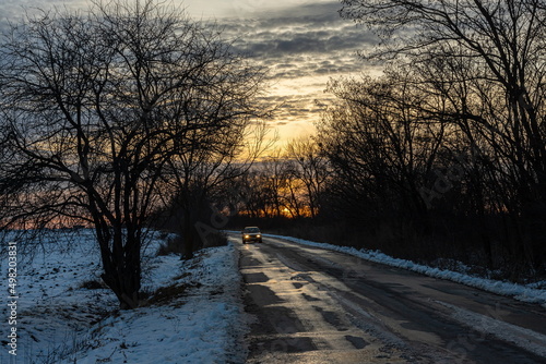 Winter road against the backdrop of a sunny sunset. Direction of movement. Car route. Sunny sunset. Morning sunrise. White snow. Evening twilight. © Oleh Marchak