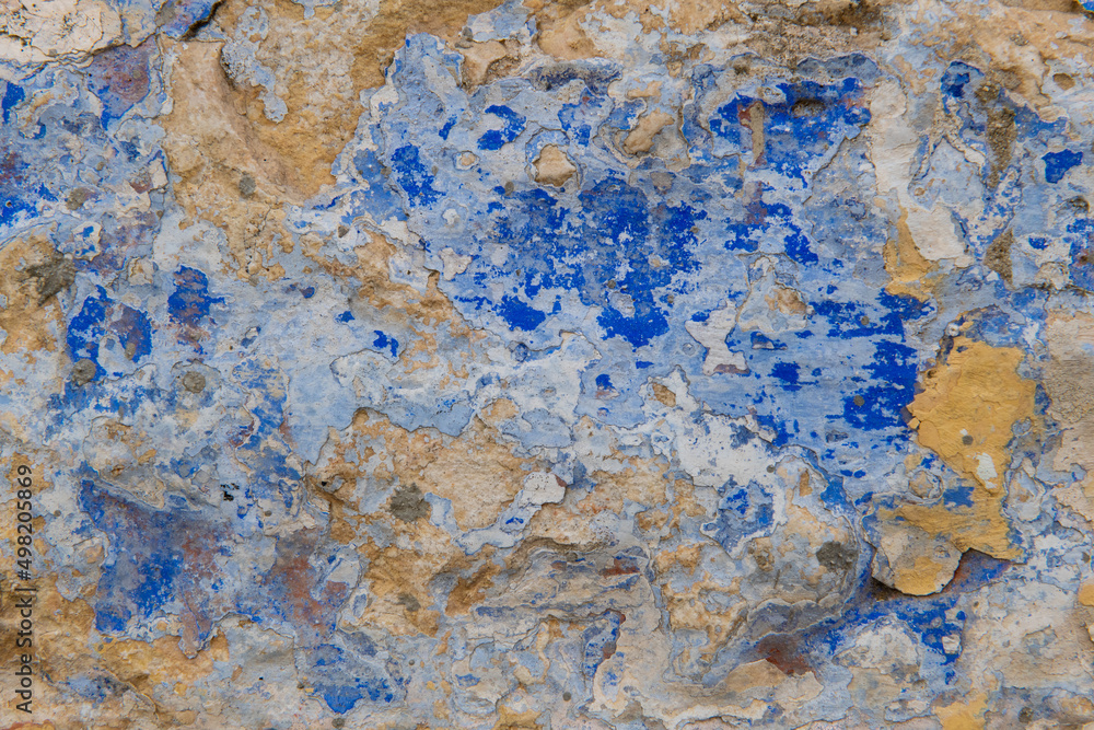 Detail of the colorful, textured exterior wall of an old, painted, peeling stucco building revealing many layers of different colored paint applied over the years.