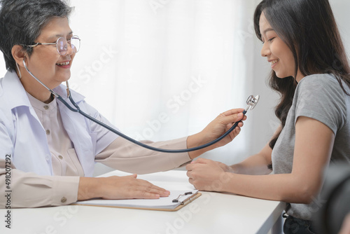 Mature, senior asian physician, psychiatrist, general woman doctor consulting concerned with young patient, using stethoscope to listen, appointment at clinic, hospital. Health care, check up medical.