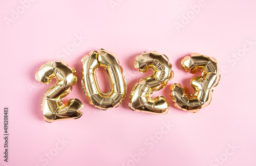 Golden inflatable numbers in the shape of 2023 on a pink background. Flat lay with place for text.