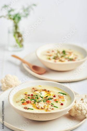 Vegan cauliflower soup on white background. Healthy vegan cauliflower soup served in bowl on white table.