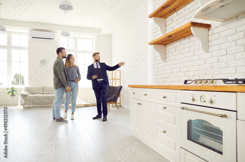 Male relator or broker show home to couple buyers or renters buying fist dwelling together. Man real estate agent demonstrate apartment to tenants. Homeowner, bank loan or mortgage, rent. photo