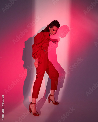 Young beautiful slender woman in a fashionable red dress with lush sleeves. Woman posing on a red background. Advertising of fashionable womens clothing.