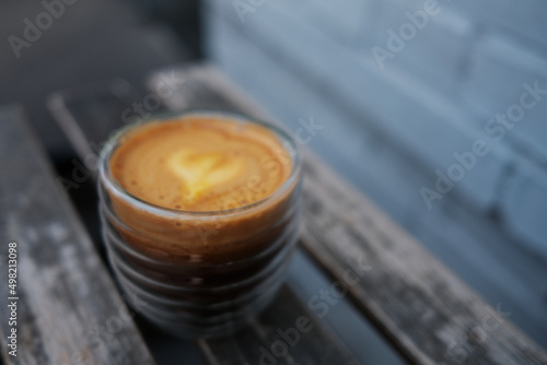 A cup of coffee stands on a wooden table against a brick wall. Focus on a drink  trendy capuorange     mix of orange juice and an espresso.