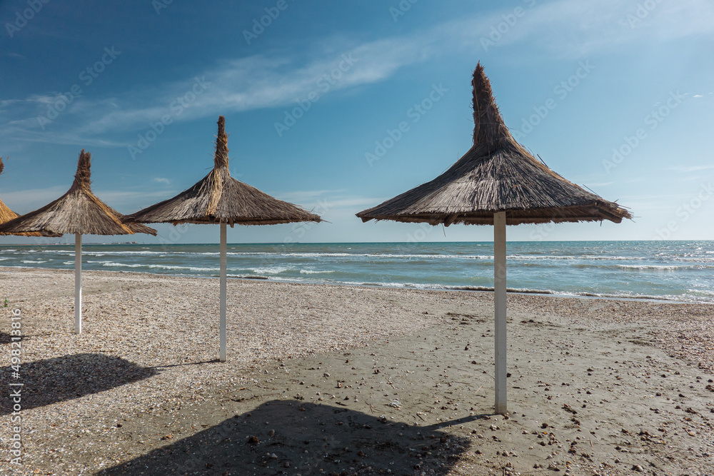 Landscape on the seaside without tourists. The view at Black Sea shore with reed umbrellas on the beach during a sunny day with blue sky. Landscape on the seaside without tourists. The view at Black Sea shore with reed umbrellas on the beach during a sunny day with blue sky.
