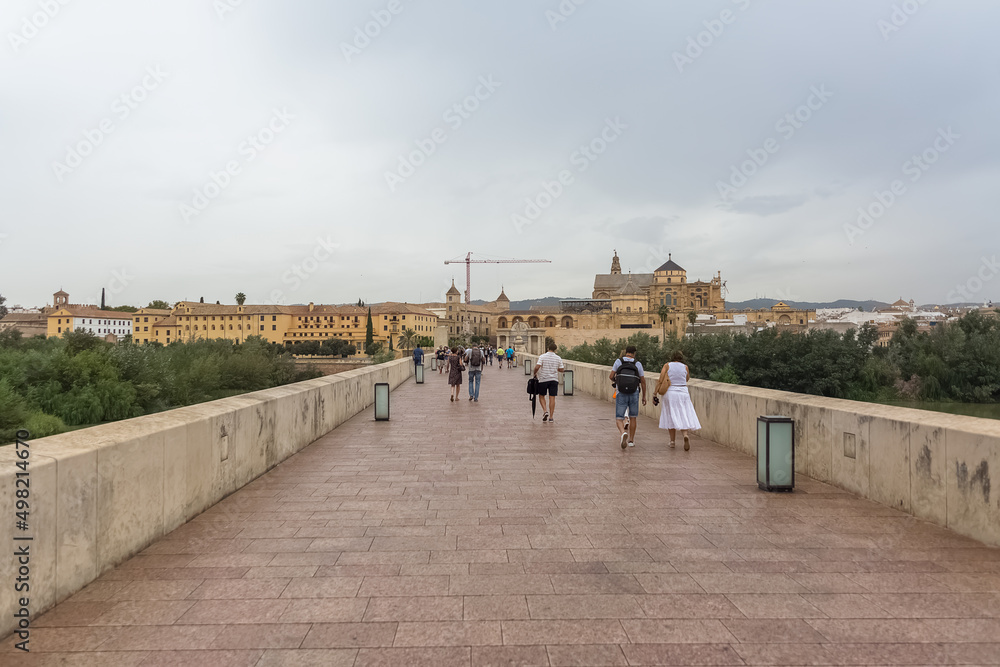 View at the Roman Bridge over Guadalquivir river, Mosque-Cathedral of Córdoba, Plaza del Triunfo as background, torurist people visiting, Cordoba downtown, Spain