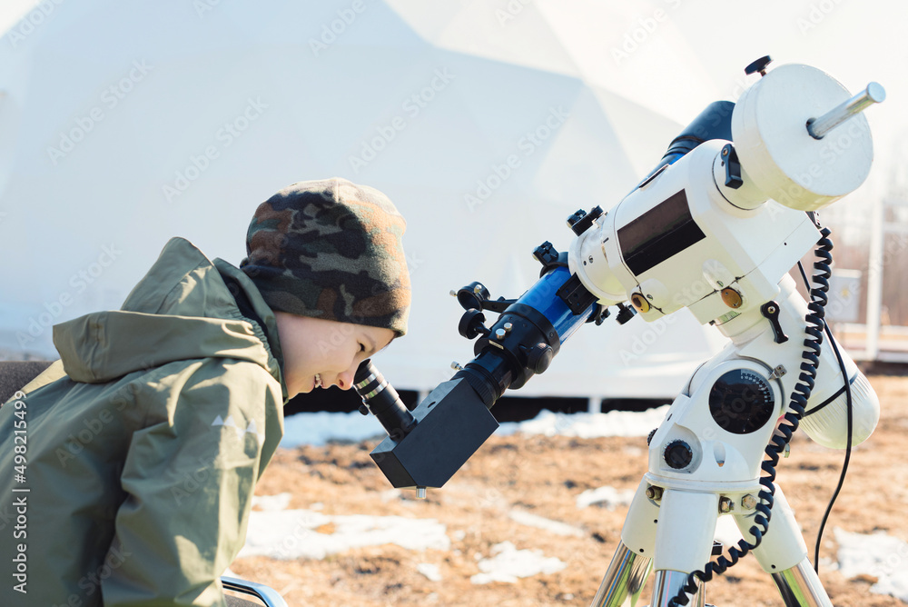 Child boy watching the sun through a telescope on a tripod at the