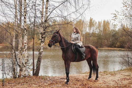Cute young woman on horse in autumn forest by lake