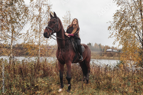 Cute young woman on horse in autumn forest by lake